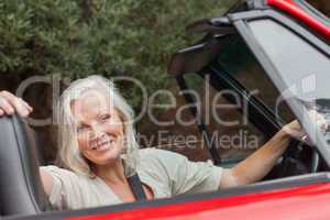 Smiling mature woman posing in red convertible