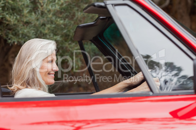 Happy mature woman driving red convertible