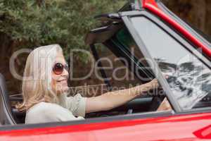 Happy mature woman with sunglasses driving red convertible