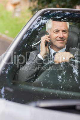 Smiling businessman on the phone driving expensive cabriolet