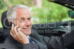 Cheerful businessman on the phone driving expensive cabriolet