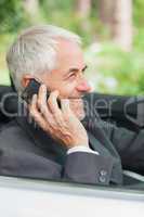 Cheerful mature businessman on the phone driving expensive cabri