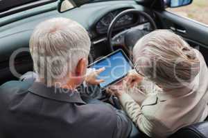 Mature partners working together on tablet in classy car