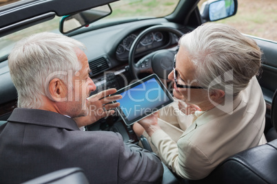 Smiling mature partners working together on tablet in classy car