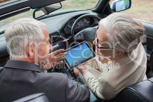 Smiling mature partners working together on tablet in classy car