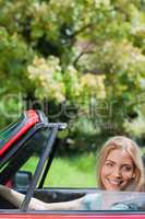 Happy blonde woman driving red cabriolet