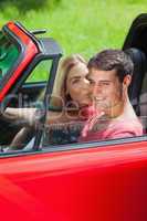Happy blonde kissing her boyfriend in red cabriolet
