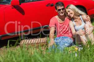 Smiling couple sitting on the grass having picnic together