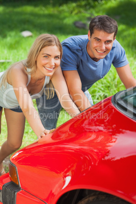 Smiling couple pushing their broken down car