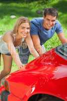 Smiling couple pushing their broken down car