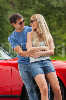 Smiling couple hugging and leaning against cabriolet