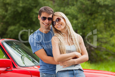 Cheerful couple hugging and leaning against cabriolet