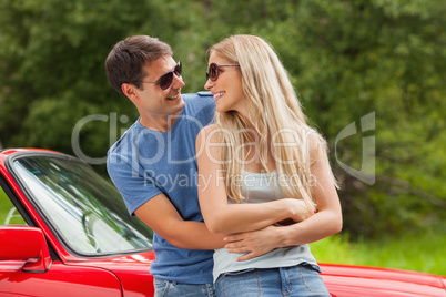 Cheerful young couple hugging and leaning against cabriolet