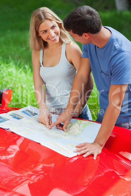 Smiling young couple reading map on their cabriolet bonnet