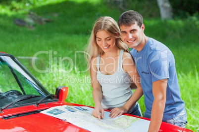 Cheerful young couple reading map on their cabriolet bonnet