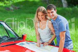 Cheerful young couple reading map on their cabriolet bonnet