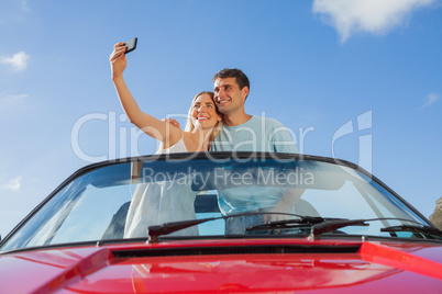 Cheerful couple standing in red cabriolet taking picture