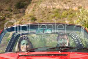 Front view of smiling couple in red cabriolet