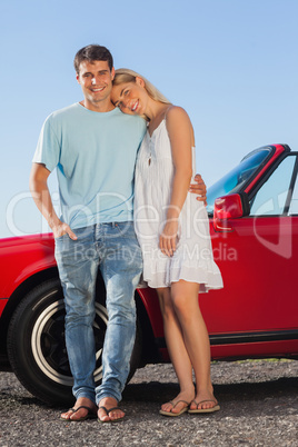 Happy cute couple posing against their red cabriolet