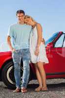 Happy cute couple posing against their red cabriolet