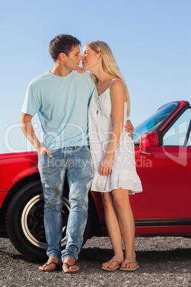 Cute couple kissing against their red cabriolet