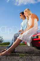 Cheerful couple sitting on their cabriolet car hood