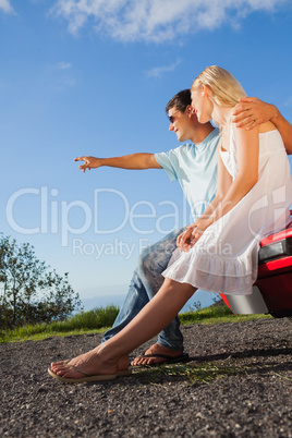 Cheerful cute couple sitting on their cabriolet car hood