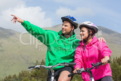 Smiling couple on a bike ride wearing hooded jumpers with man po