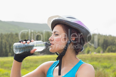Athletic woman wearing bike helmet drinking water