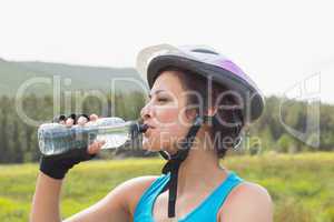 Athletic woman wearing bike helmet drinking water