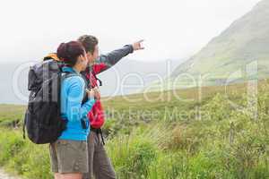 Couple of hikers with backpacks pointing at mountain