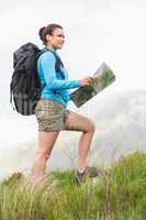 Attractive hiker with backpack walking uphill holding a map