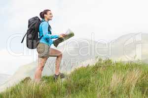 Attractive hiker with backpack hiking uphill holding a map