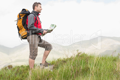 Handsome hiker with backpack hiking uphill holding a map