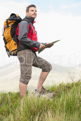 Handsome hiker with rucksack walking uphill holding a map