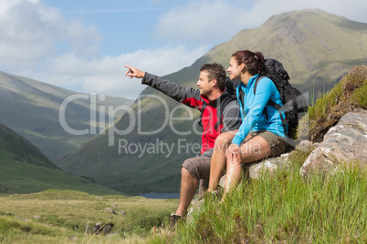Couple taking a break after hiking uphill with man pointing