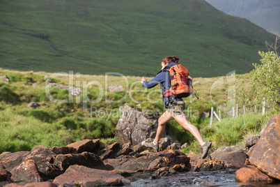 Athletic hiker leaping across rocks in a river