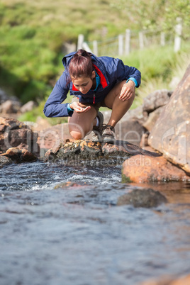 Hiker bending to take a drink from the stream