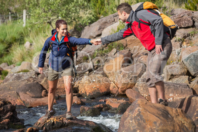 Man helping his smiling girlfriend to cross a river