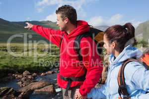 Couple standing at edge of river on a hike with man pointing