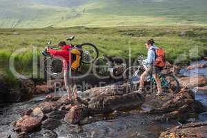Couple crossing a river holding their bikes