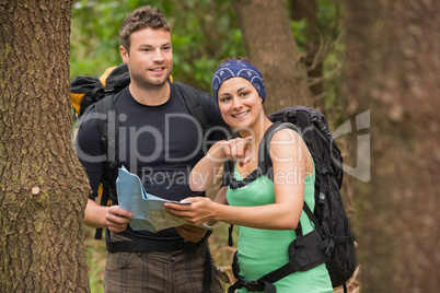 Fit couple reading map in a forest with woman pointing