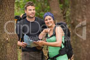 Fit couple reading map in a forest with woman pointing