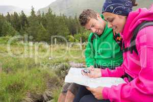 Couple sitting on a rock resting during hike using map and compa