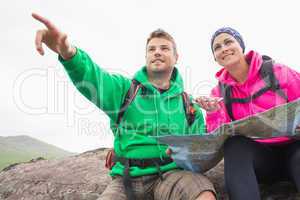 Couple using map and compass sitting on a rock with man pointing