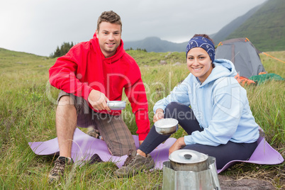 Couple cooking outside on camping trip smiling at camera