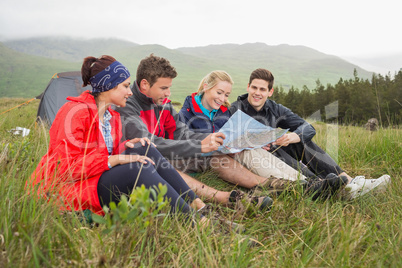 Friends sitting on grass and looking at map on camping trip