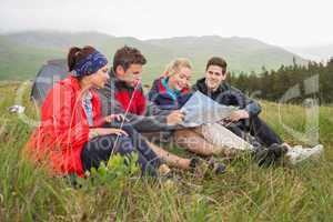 Friends sitting on grass and looking at map on camping trip