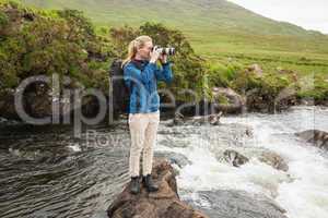 Blonde woman standing on a rock in a stream taking a photo