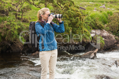 Blonde standing on a rock in a stream taking a photo